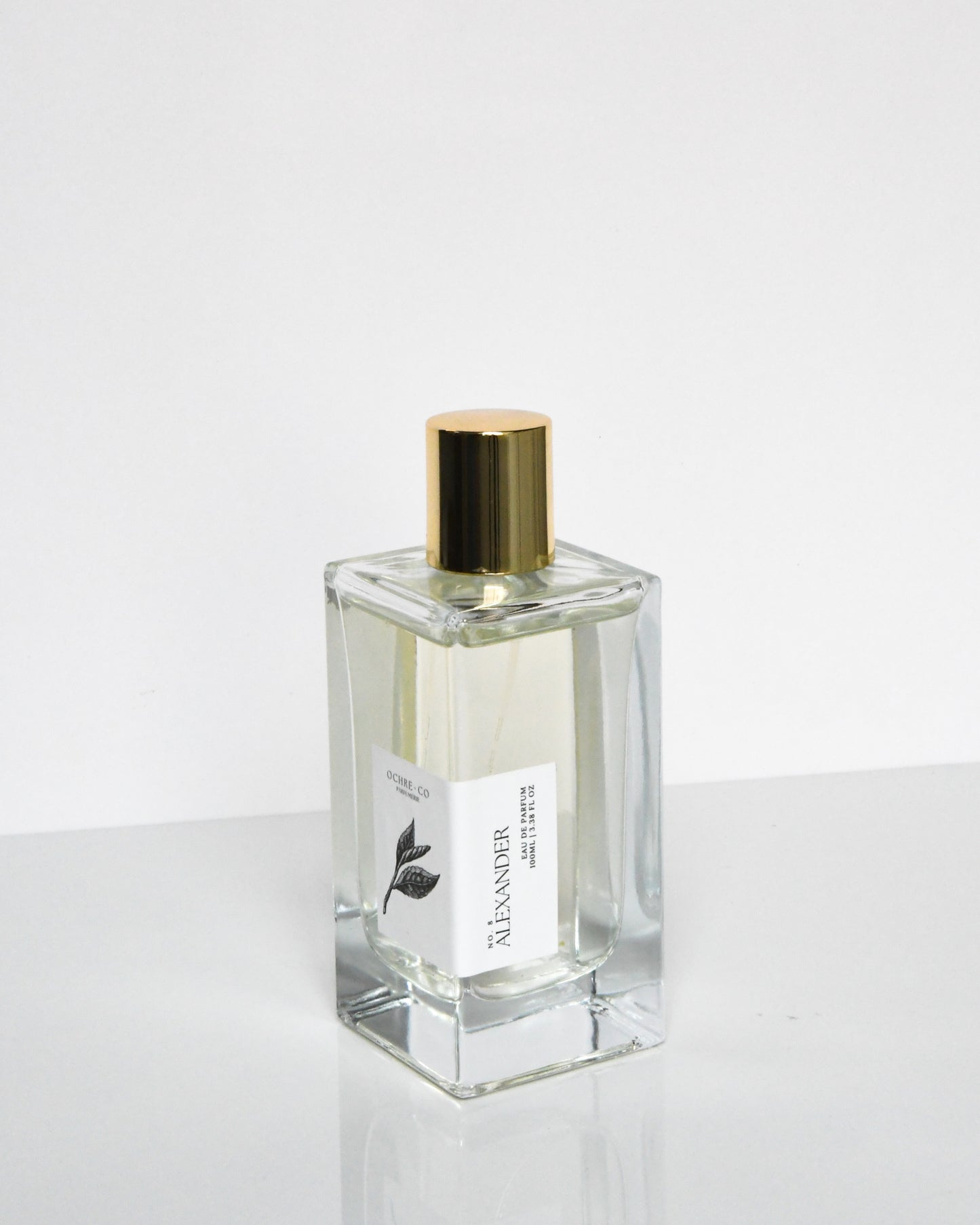 A clear glass bottle of 'Alexander - Eau de Parfum' with a gold-colored cap, positioned against a white background.