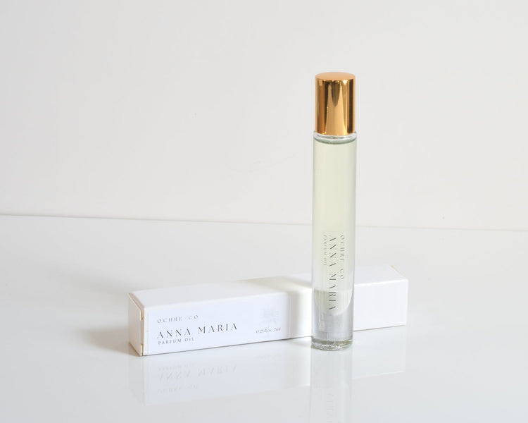 A bottle of Anna Maria perfume oil with a clear liquid and a gold-colored cap, placed on a white surface.