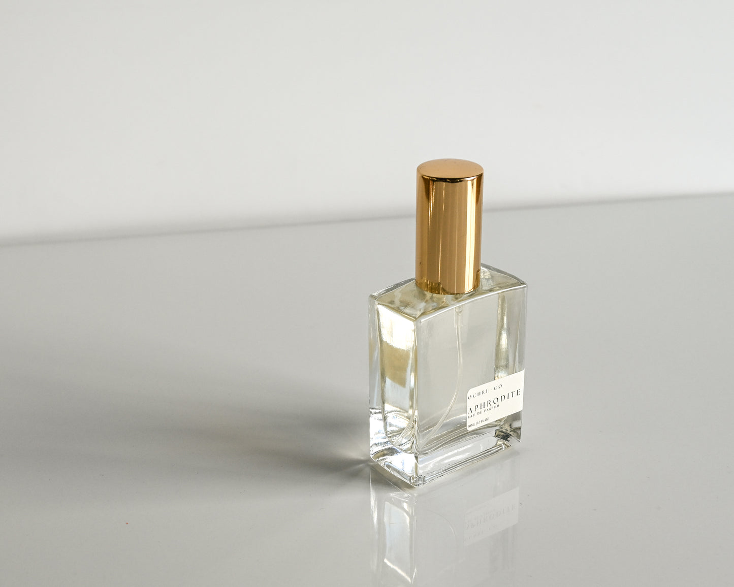 Clear perfume bottle with gold cap on a reflective surface