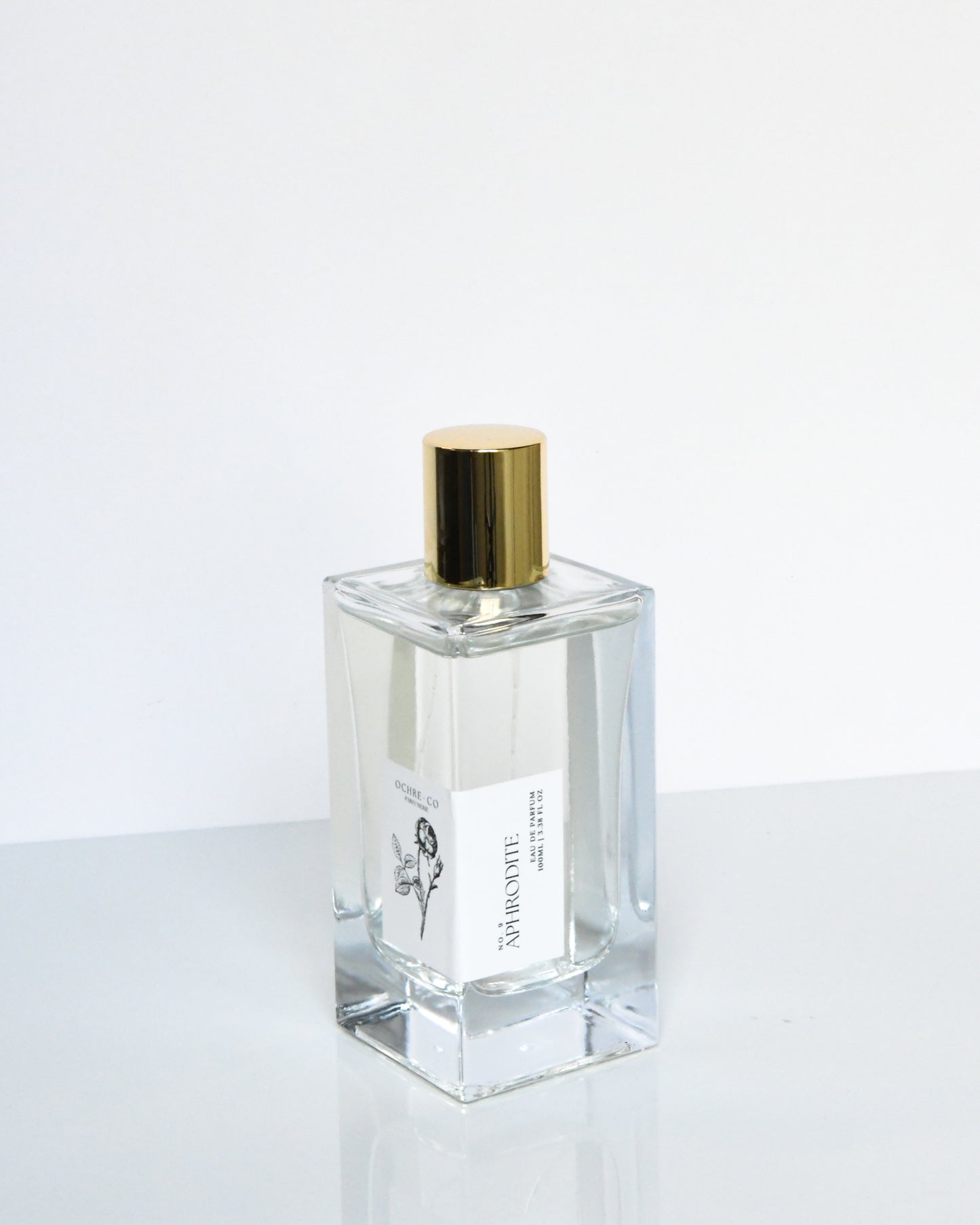 A clear glass bottle of 'Aphrodite - Eau de Parfum' with a gold-colored cap, labeled with the product name and brand.
