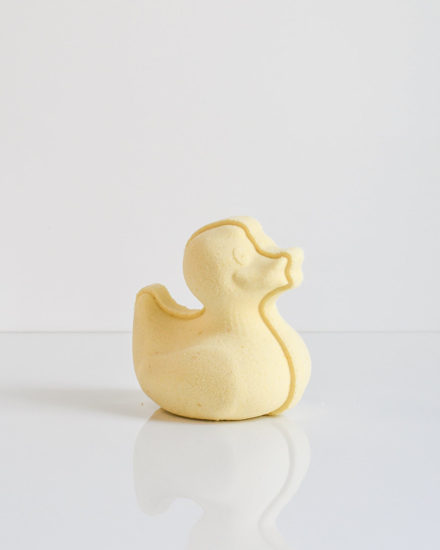 A yellow bath bomb shaped like a duckie on a white background