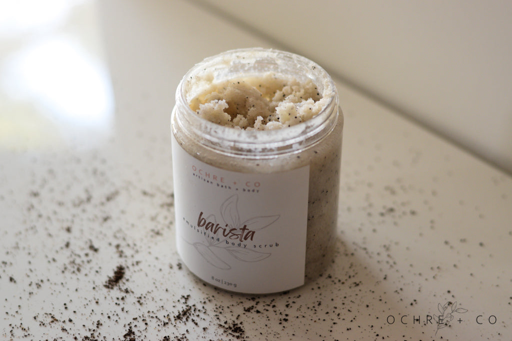 Barista sugar scrub in an open jar, showcasing the texture, with a white background and scattered coffee grounds