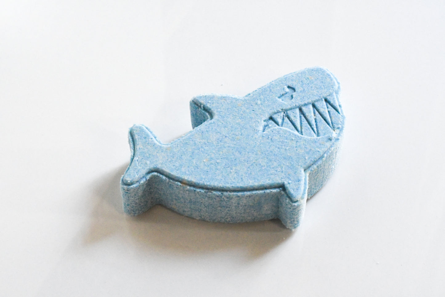 A bright blue shark-shaped bath bomb on a white background