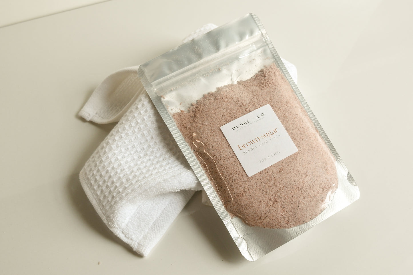 Packaged soft brown bubbling bath salt powder on a white background