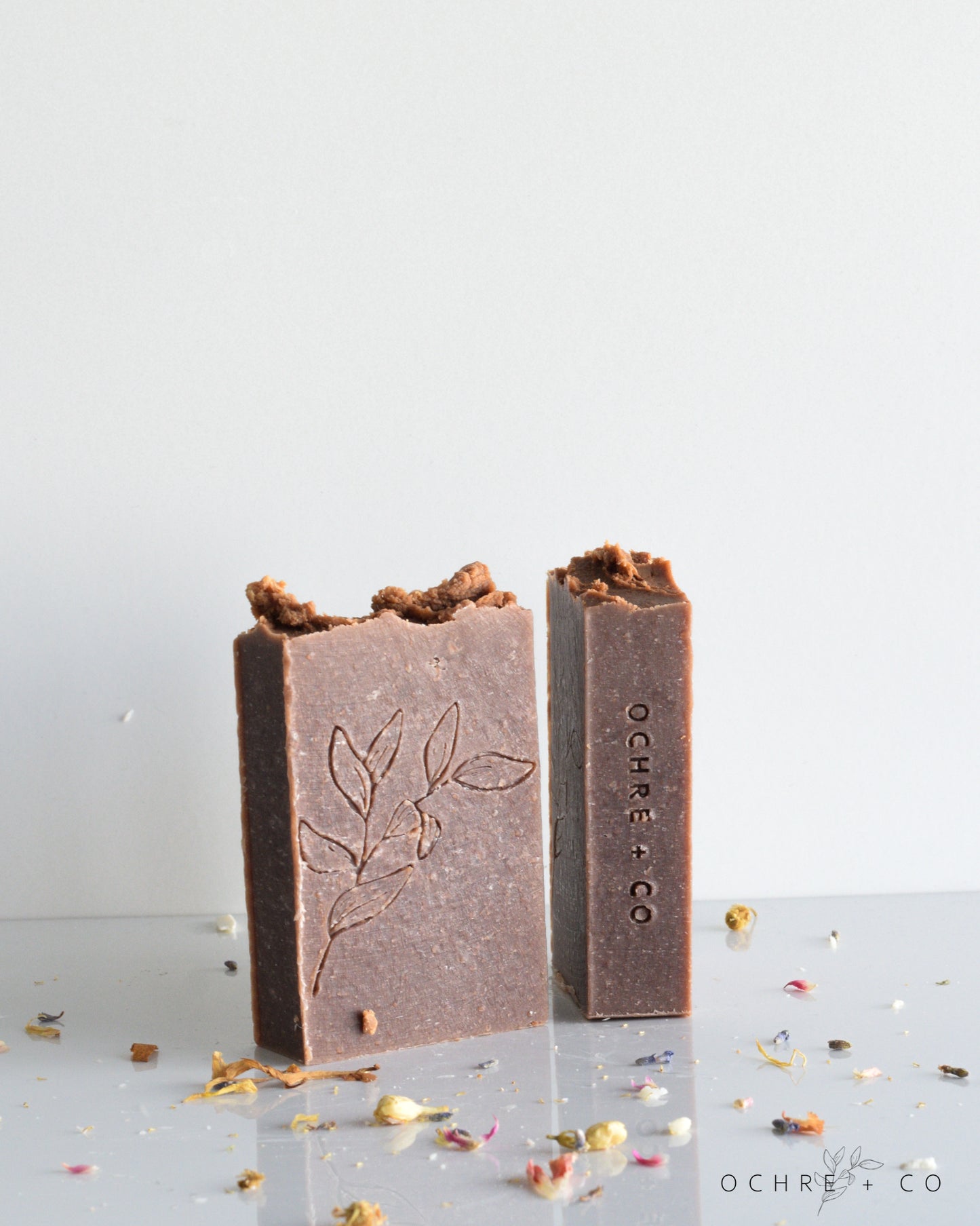 Two dark brown soap bars on a white background with scattered dried florals