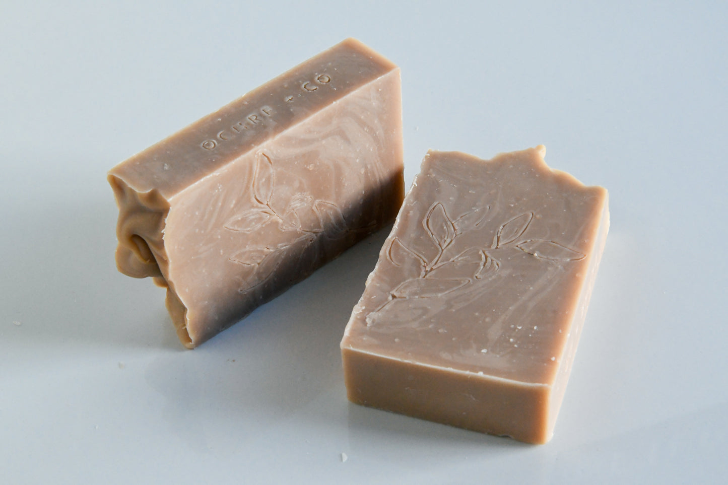 Two soft beige bar soaps with a cinnamon amber scent laying with a white background.