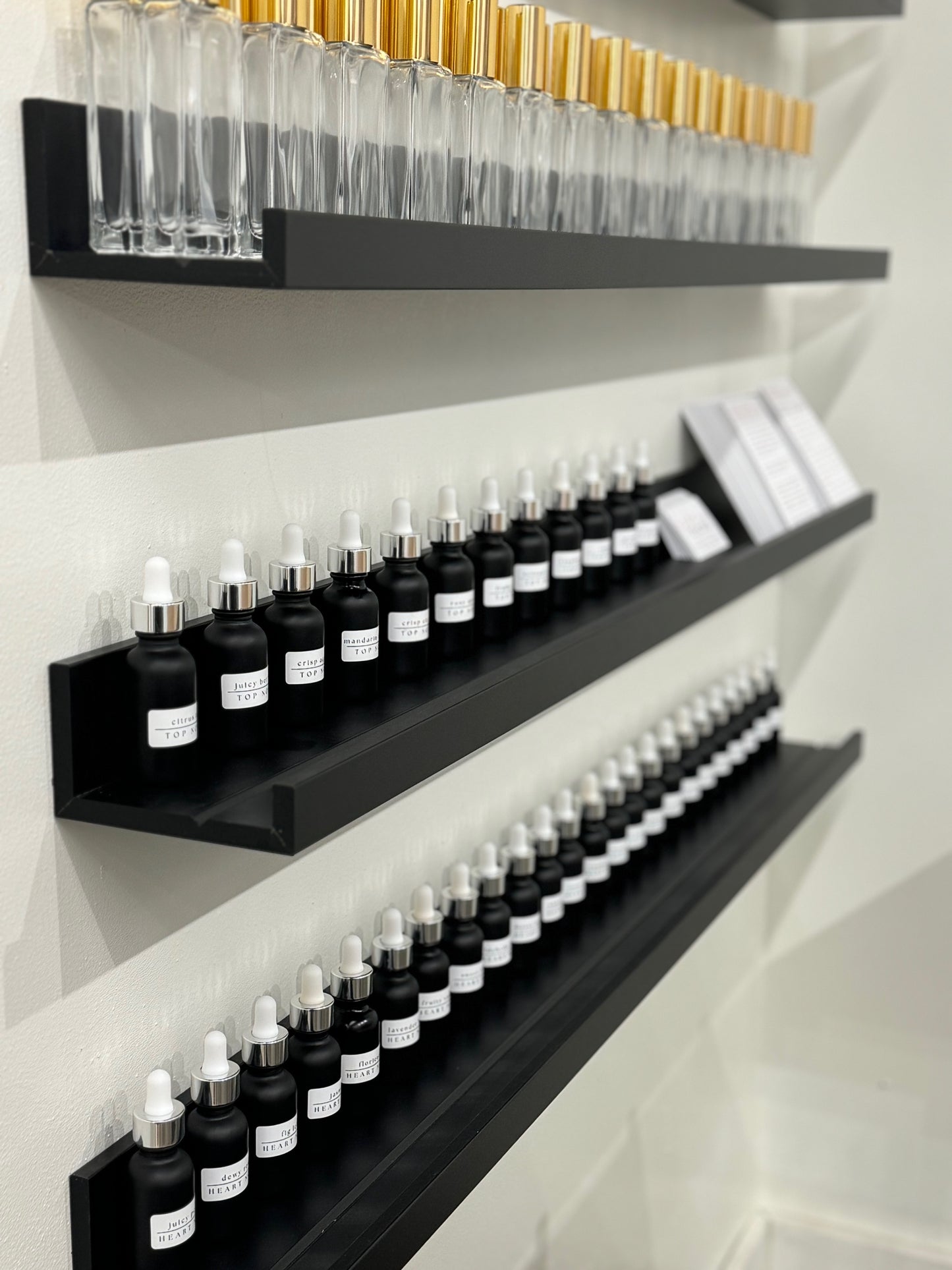 A wall-mounted shelf with multiple perfume bottles labeled with various scents, set against a white background.