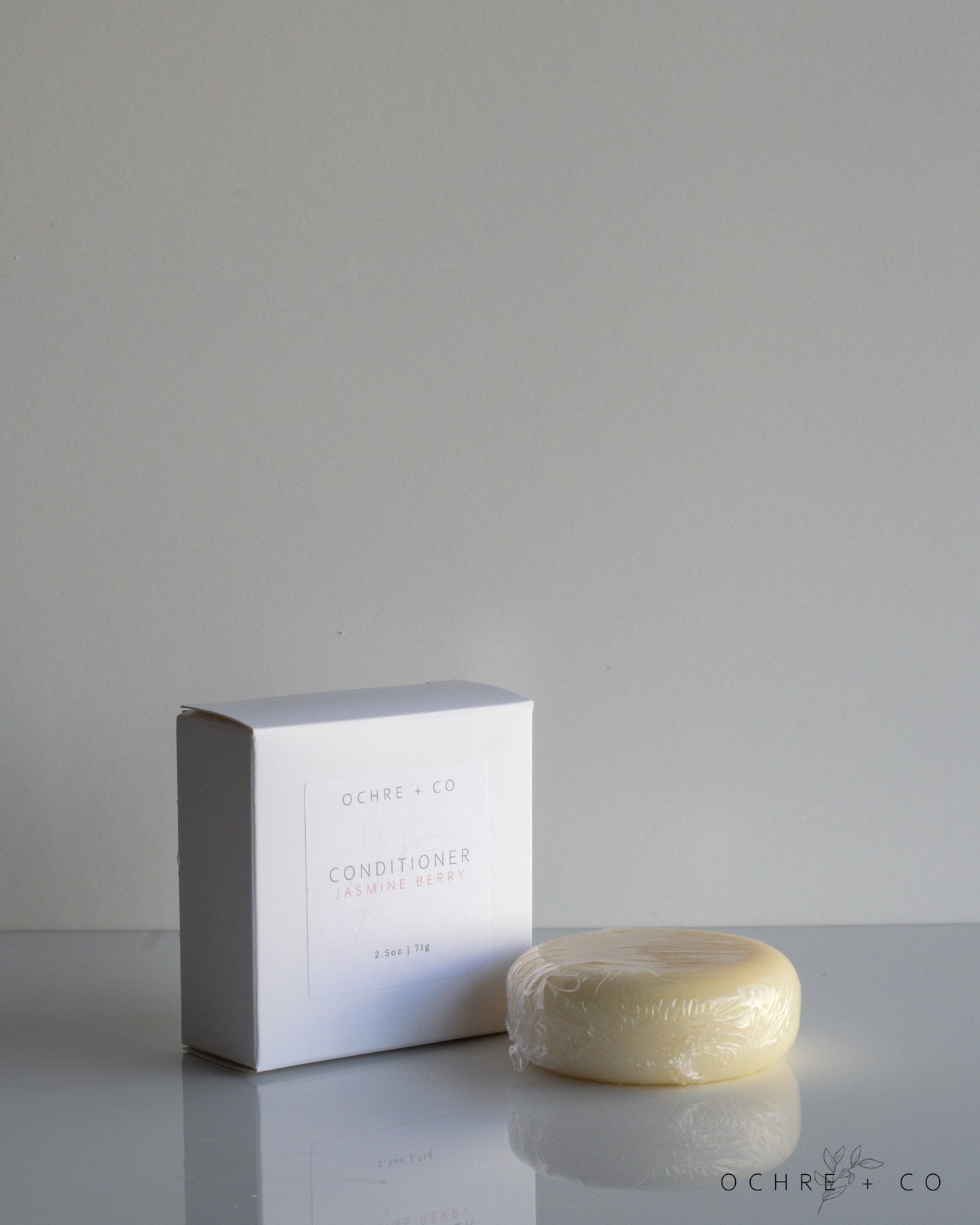 A conditioner bar next to its packaging box, labeled 'JASMINE BERRY'. The background is neutral and the product is in the foreground.