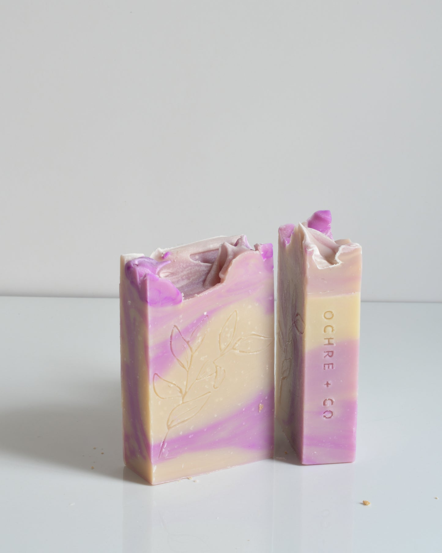 Two purple and creamy white swirled bars of soap standing up on a white background