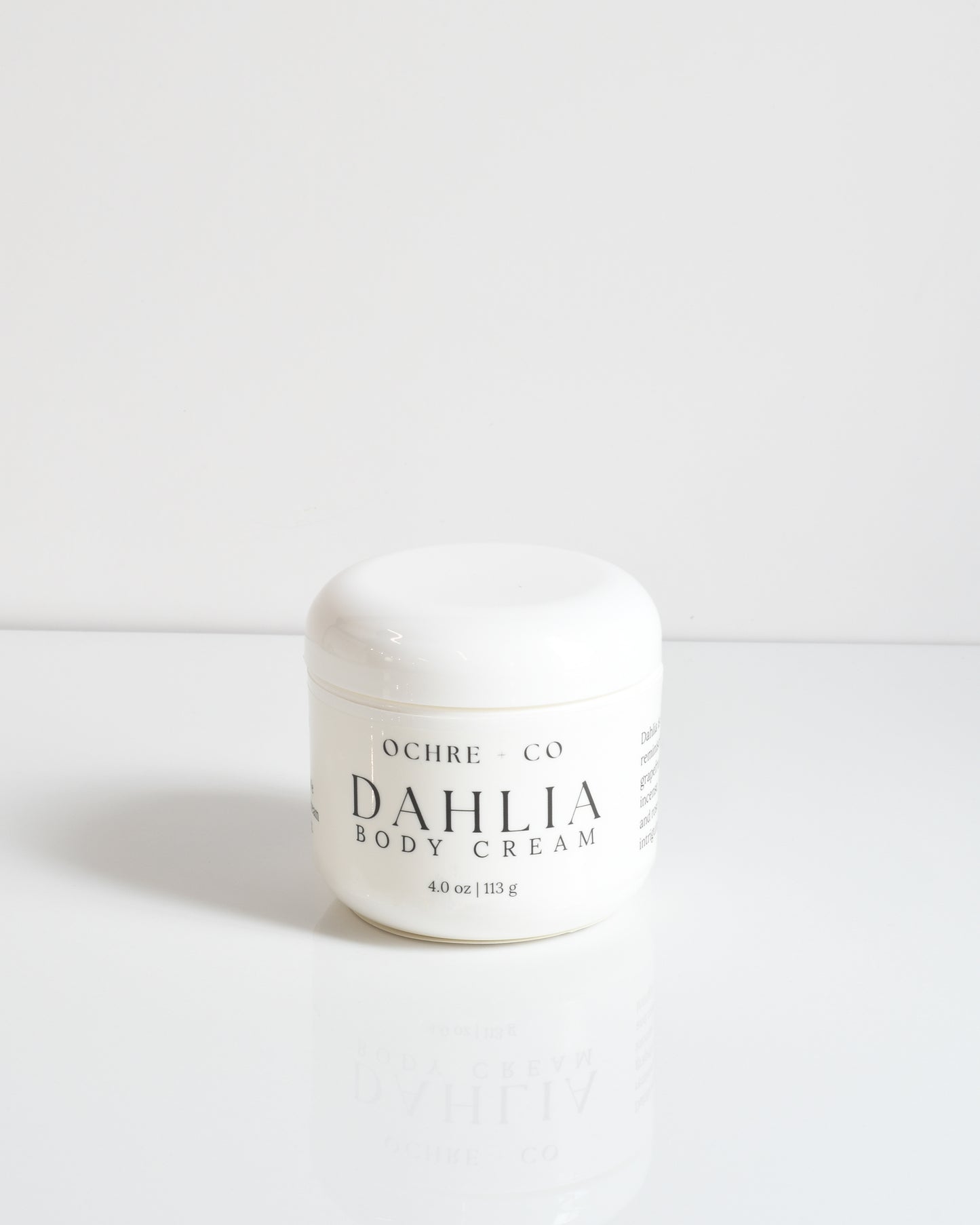 A white jar of Dahlia Body Cream by Ochre + Co. with a lid, on a white background.