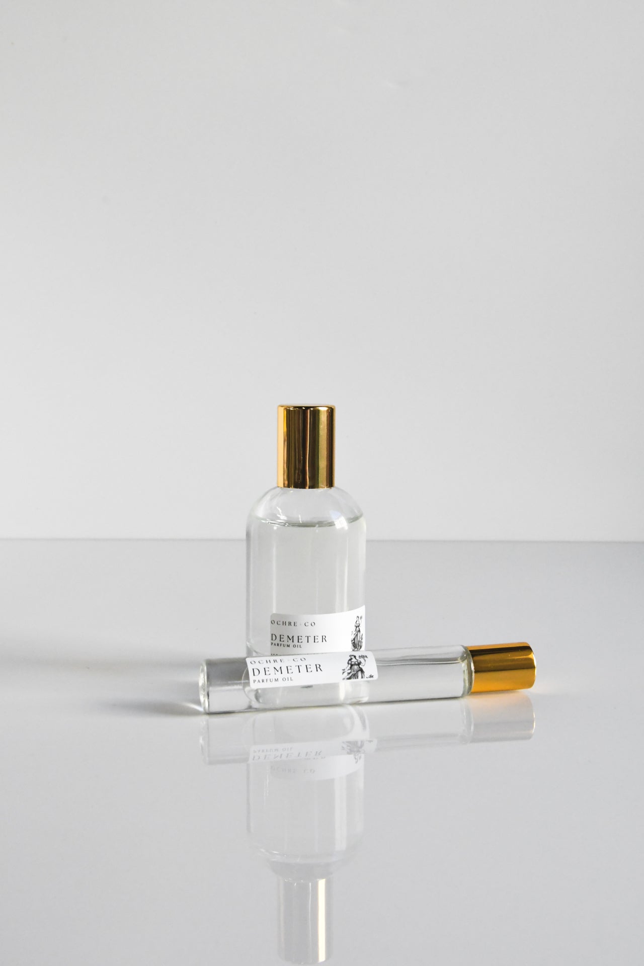 two different sizes of Demeter perfume oil in glass bottles with gold lids on a white background