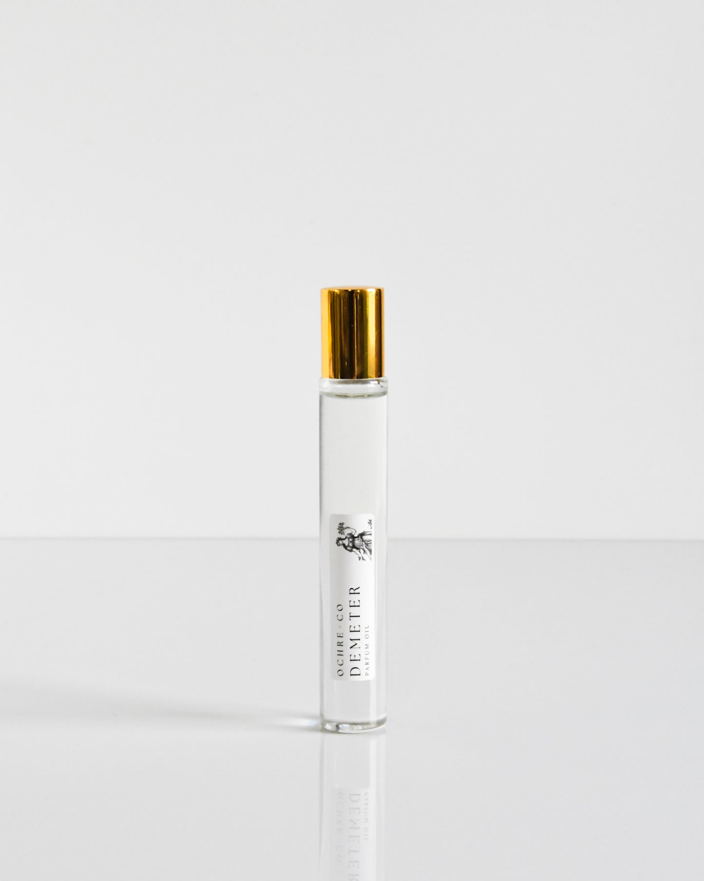 A clear glass bottle of Demeter perfume oil with a gold-colored cap, labeled with the brand name.