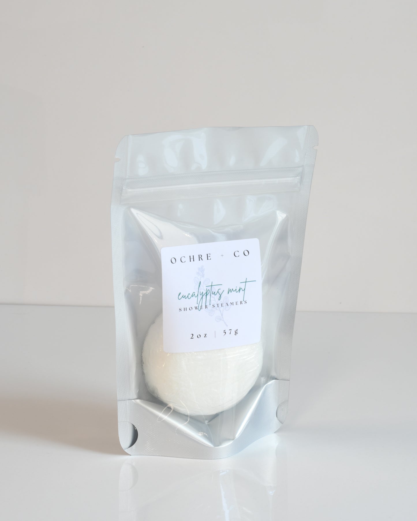 A shower steamer packaged in a clear plastic pouch with a label, displaying a white tablet meant for use in showers.