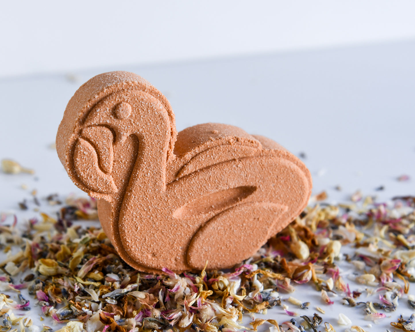 An orange bath bomb designed to look like a flamingo, with decorative dried florals around it on a white background.