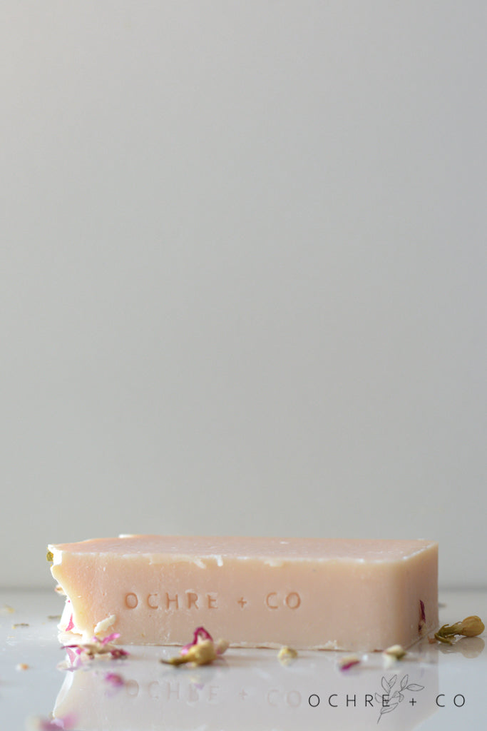 A soft pink soap bar lying on a white background with scattered dried florals