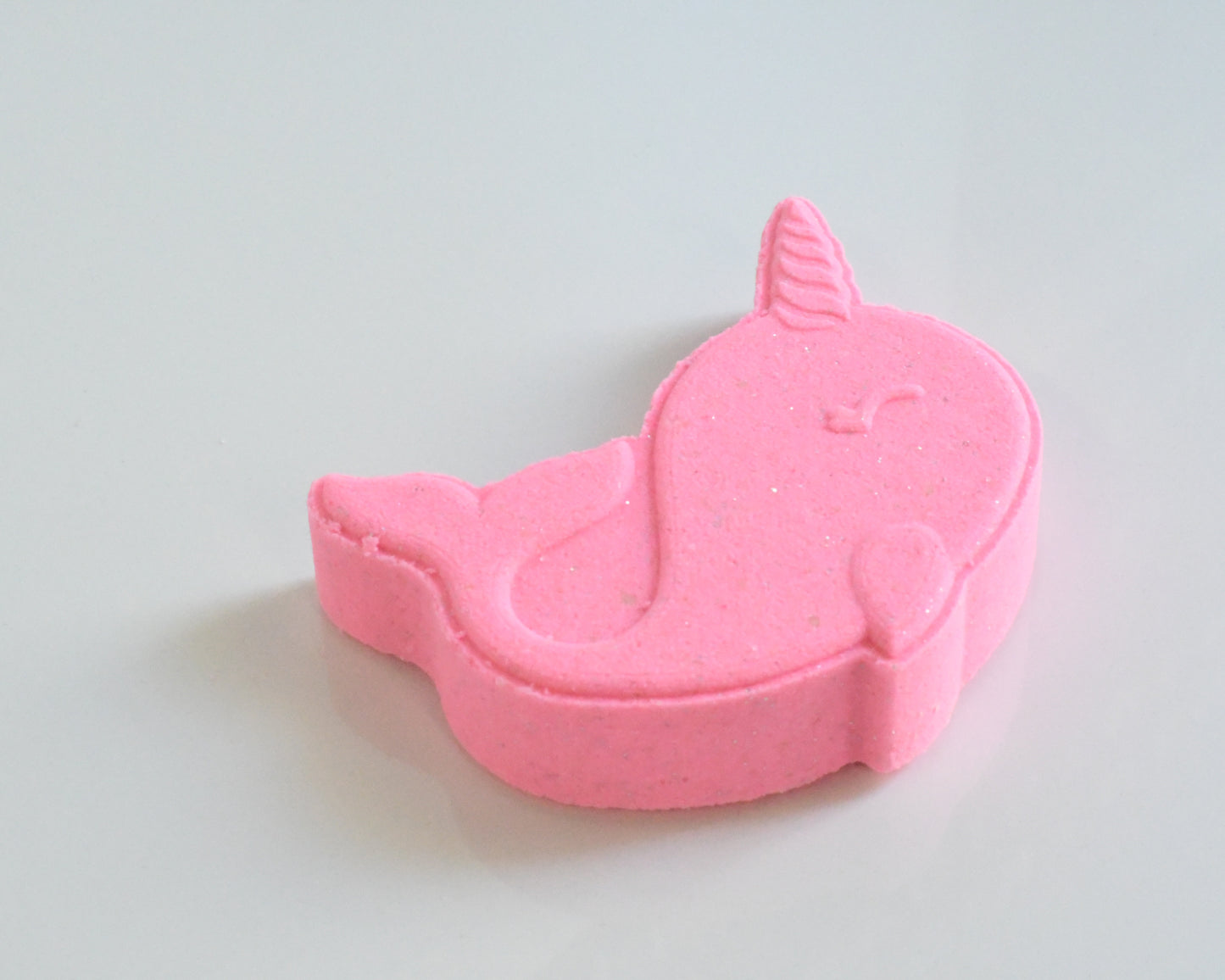 A bright pink narwhal-shaped bath bomb on a white background
