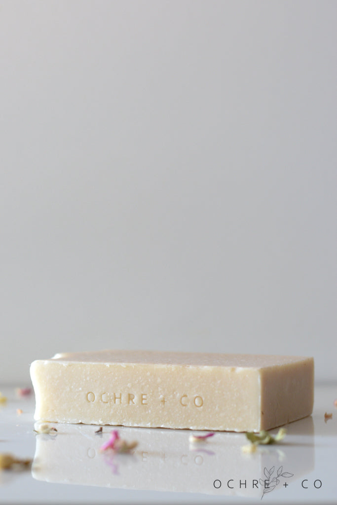 A creamy white soap bar lying on a white background with scattered dried florals