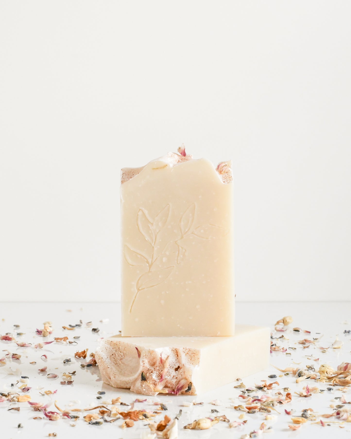 Two Jasmine Honey soap bars on a white background with scattered dried florals, one standing on top of the other