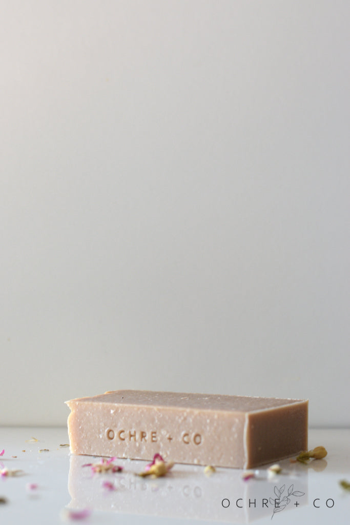 A soft brown soap bar lying on a white background with scattered dried florals