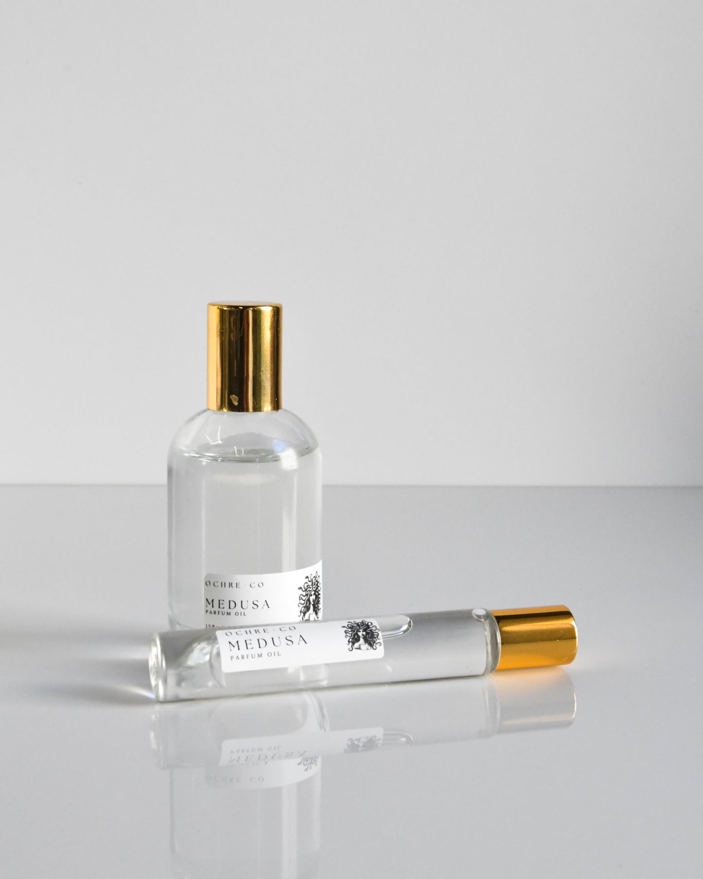 Two different sizes of Medusa perfume oil in clear glass bottles with gold caps on a white background