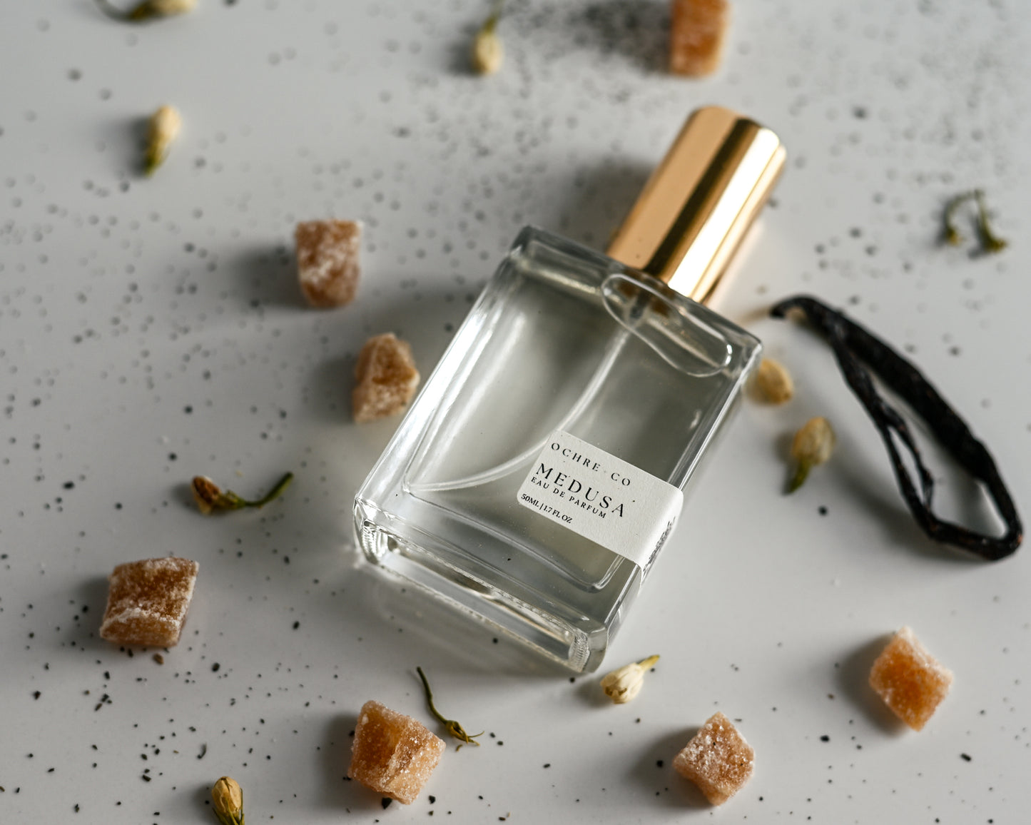Perfume bottle labeled 'Medusa' on a textured surface with scattered ingredients.