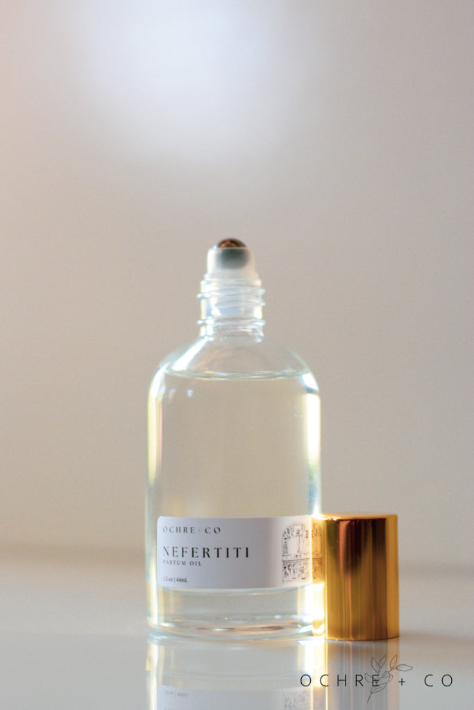 A clear glass bottle of Nefertiti perfume oil with a gold-colored cap, labeled with the brand name and product name.