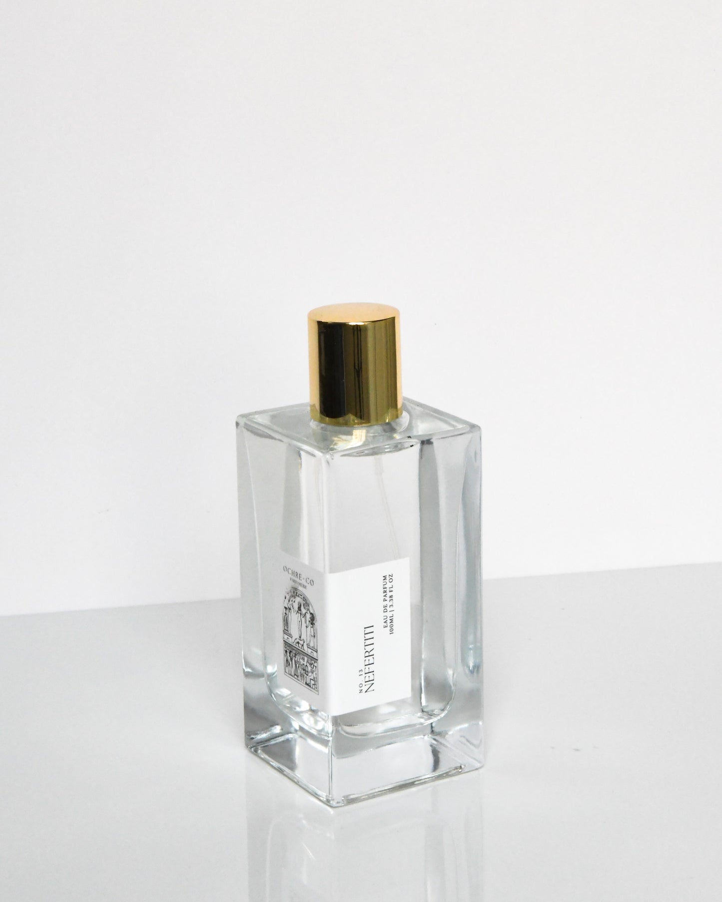 A clear glass bottle of Nefertiti Eau de Parfum with a gold-colored cap.