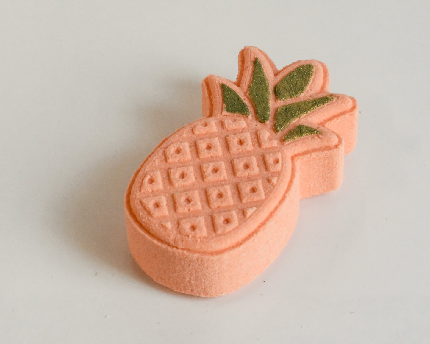 A bath bomb shaped like a pineapple with a orange base and green top, on a white background.