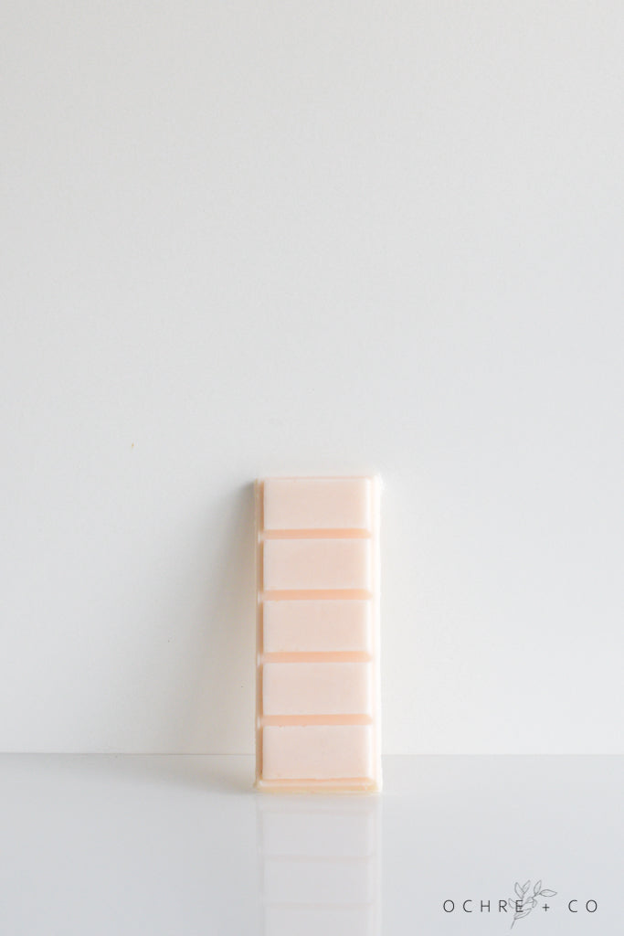 A stack of pale peach-colored wax tarts on a white surface with a white background.