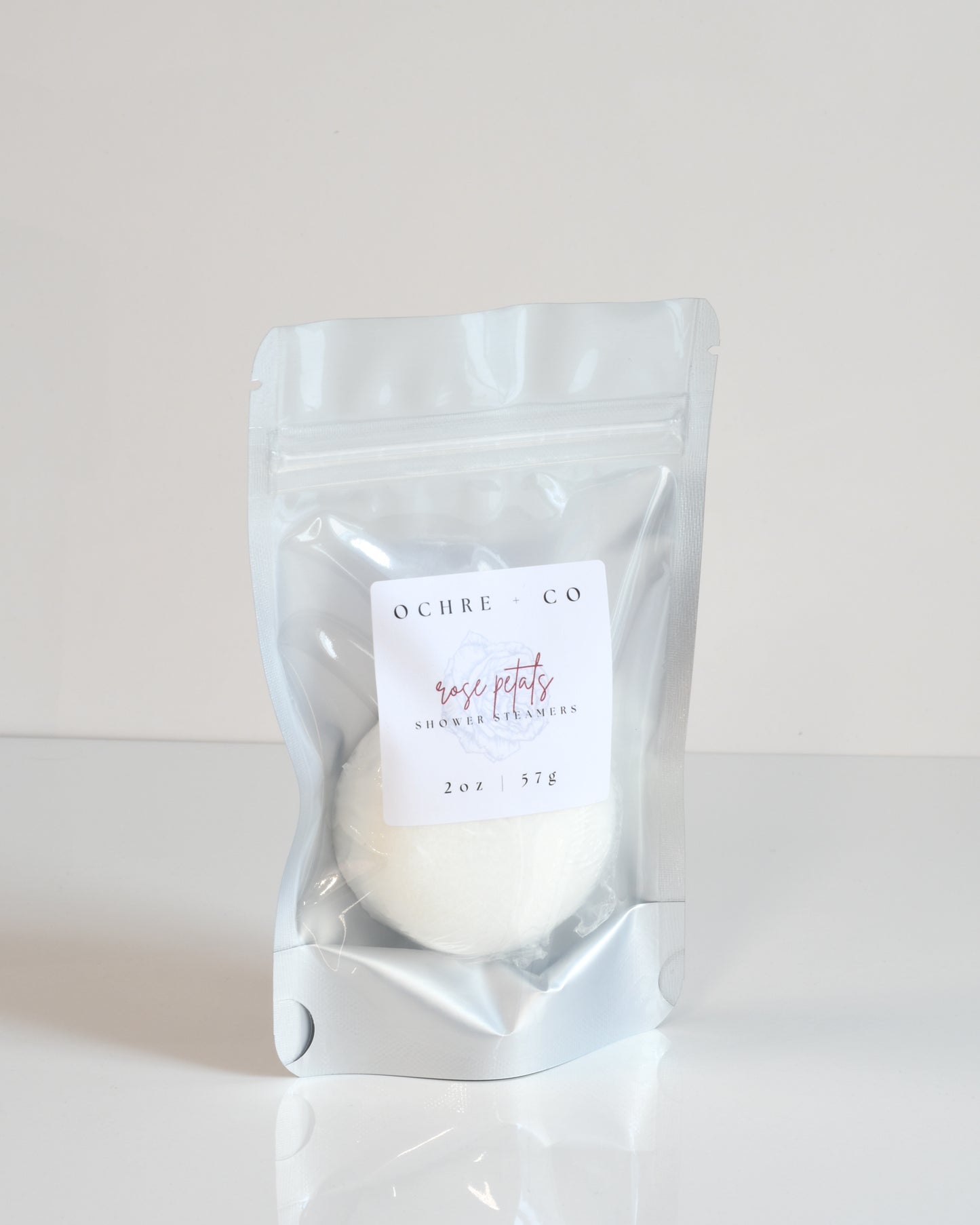 A shower steamer packaged in a clear plastic bag with a label reading 'ROSE PETALS'