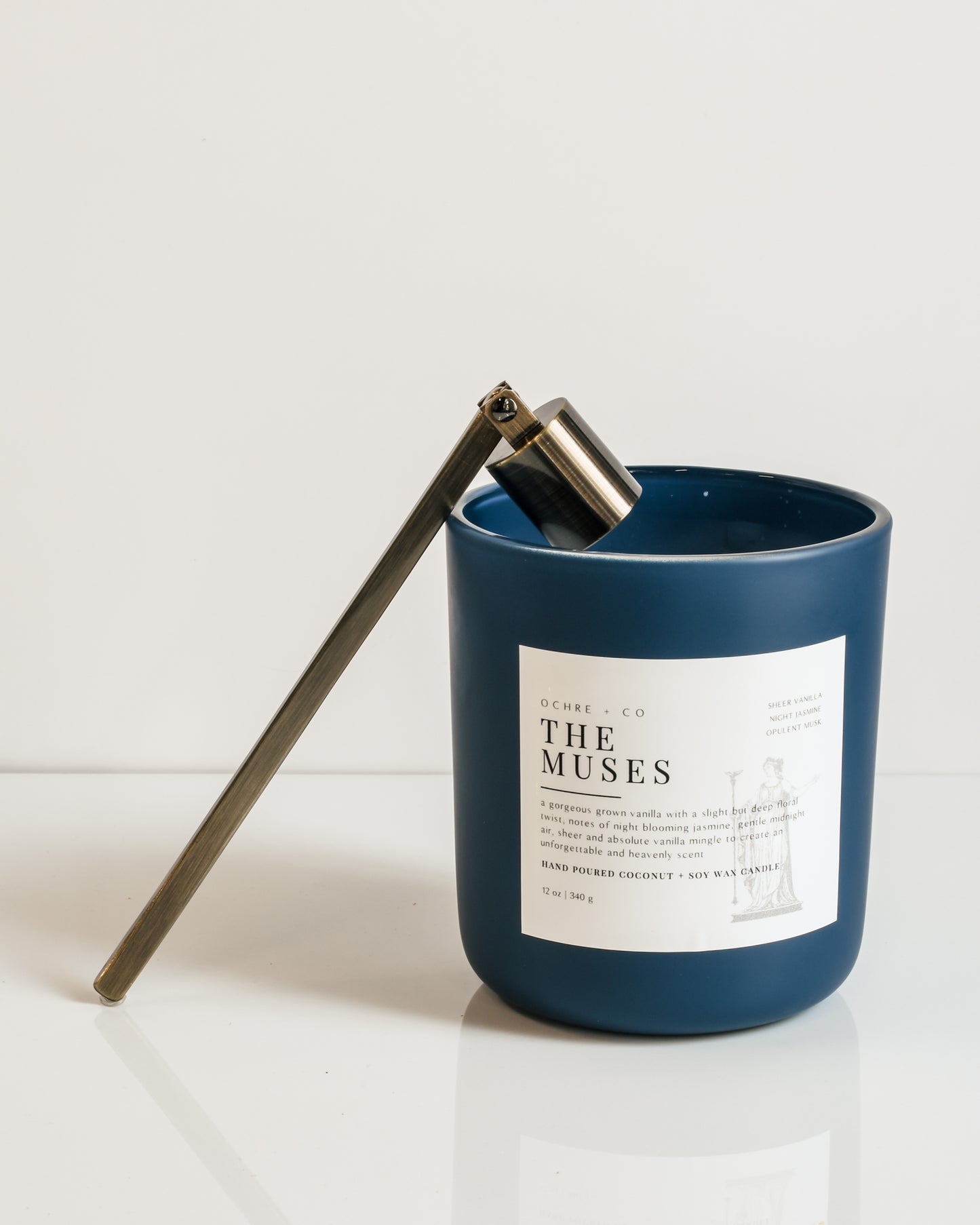 A rubbed bronze candle snuffer posed on The Muses' navy candle vessel