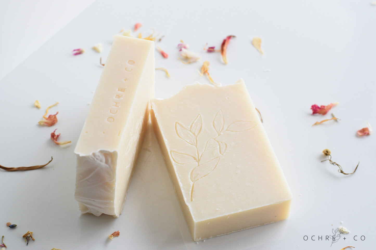 Two bars of white patchouli soap laying on a white background with scattered dried florals