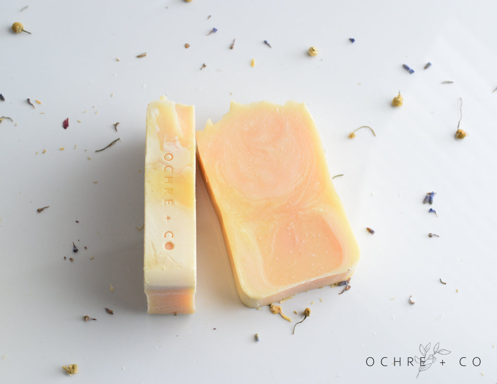 Two yellow and white bars of soap laying on a white background with scattered dried florals