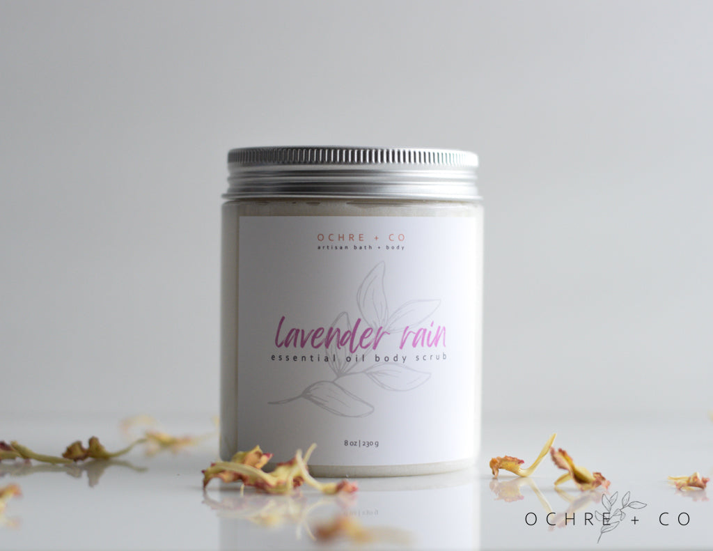 Lavender Rain essential oil sugar scrub in a jar with a white background and scattered dried florals
