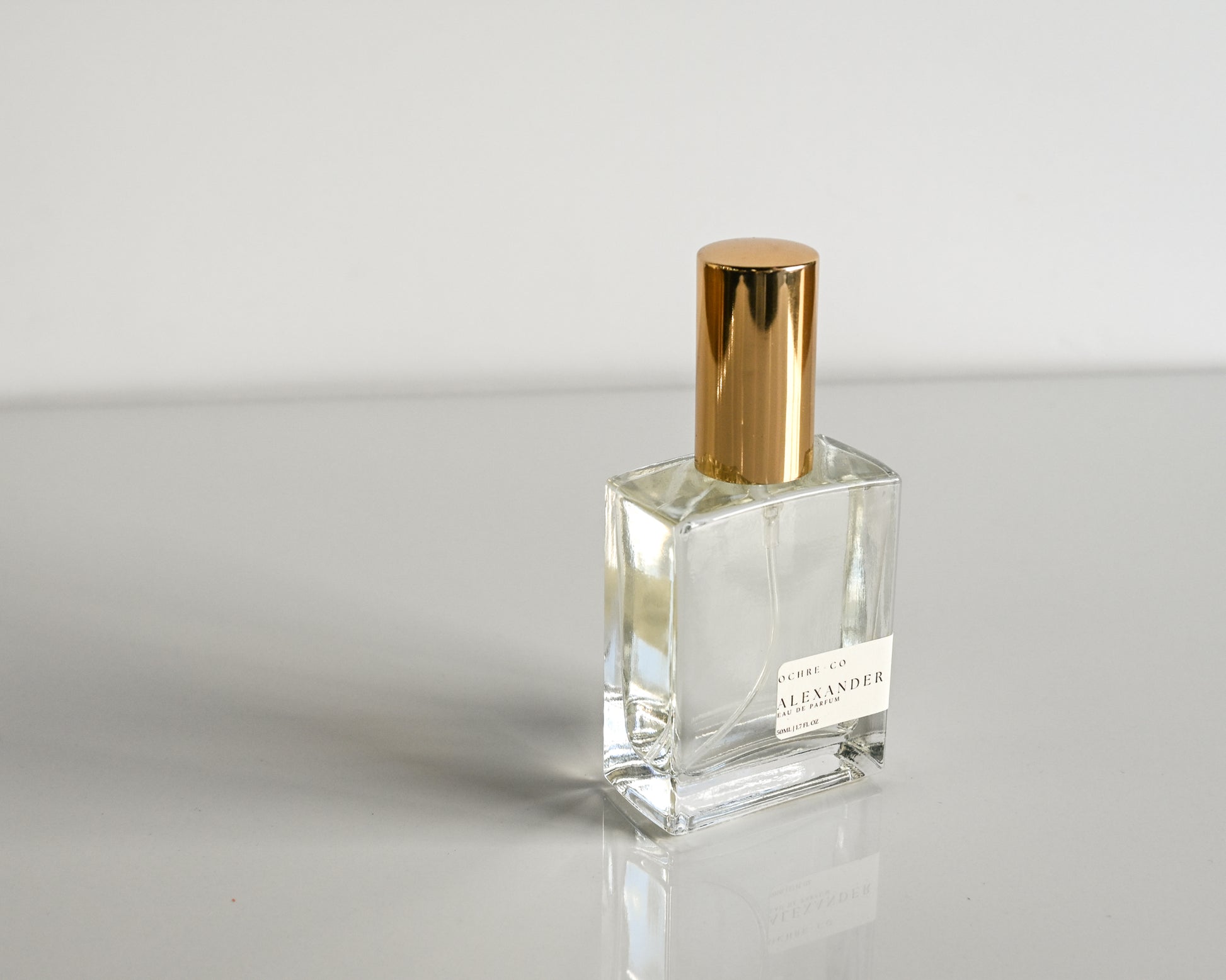 Clear perfume bottle with gold cap on a light gray background