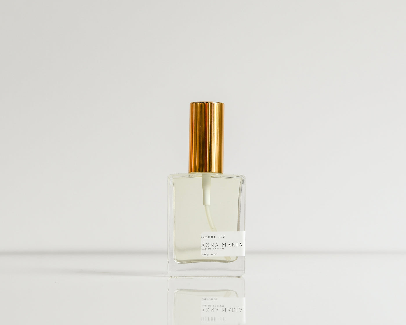 A clear glass perfume bottle with gold cap on a white background named "ANNA MARIA"