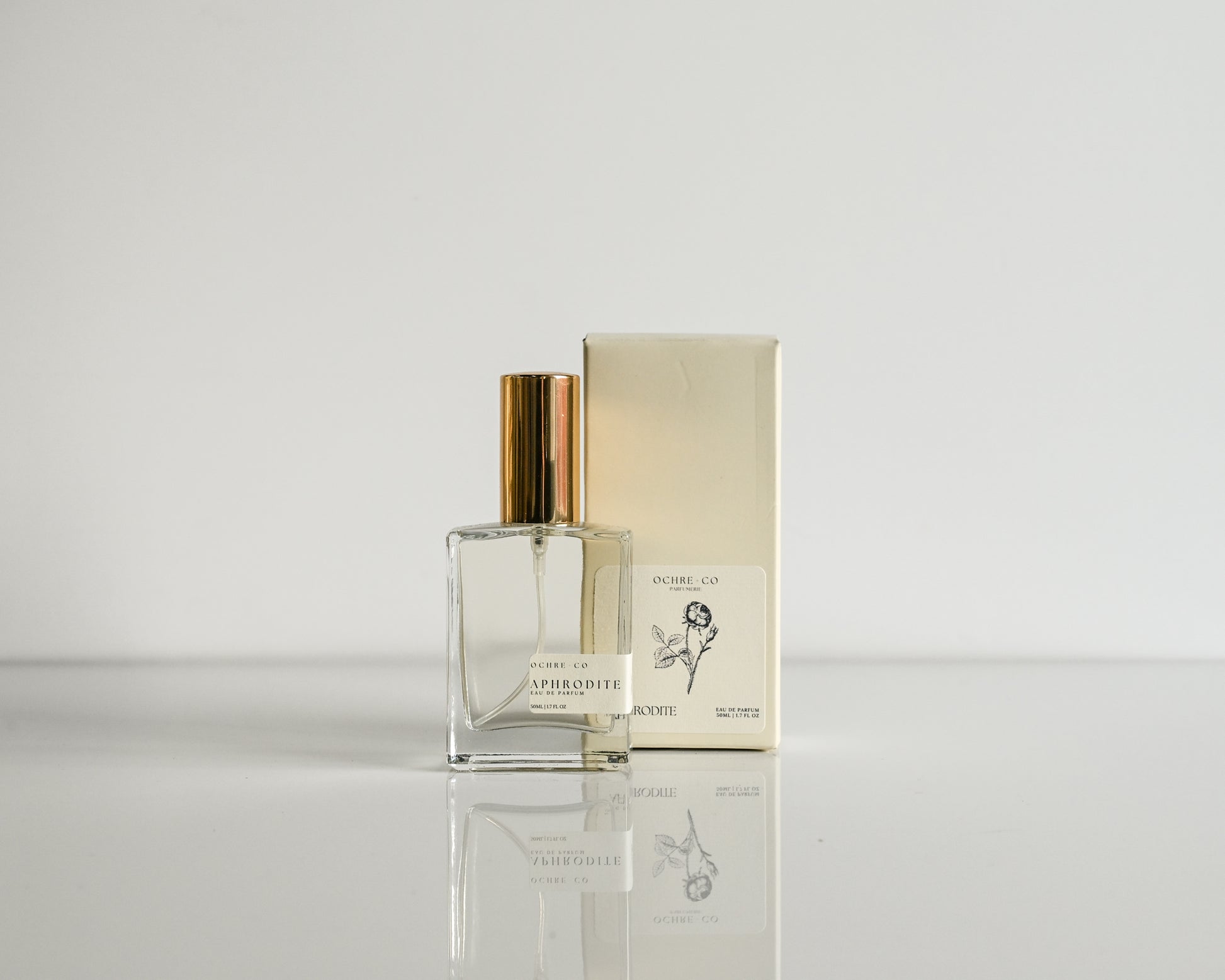 Perfume bottle with gold cap and packaging on a reflective surface with a light gray background