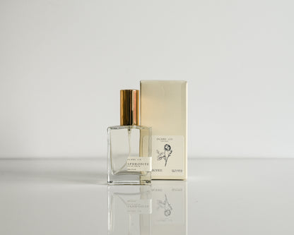 Perfume bottle with gold cap and packaging on a reflective surface with a light gray background