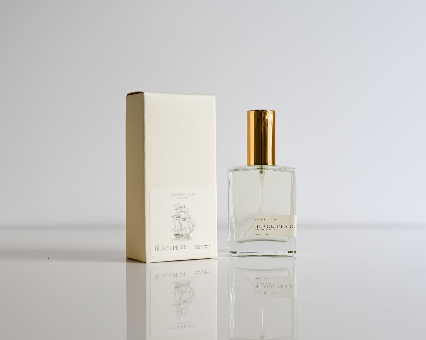Perfume bottle of Black Pearl with its box with gold cap and white box on a light gray background