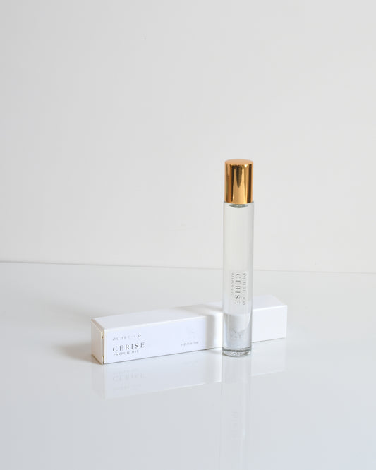 A clear bottle of perfume oil with a gold-colored cap, labeled 'Cerise', placed on a white surface.