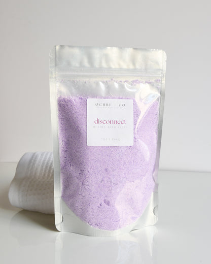 Packaged light lavender bubbling bath salt powder on a white background
