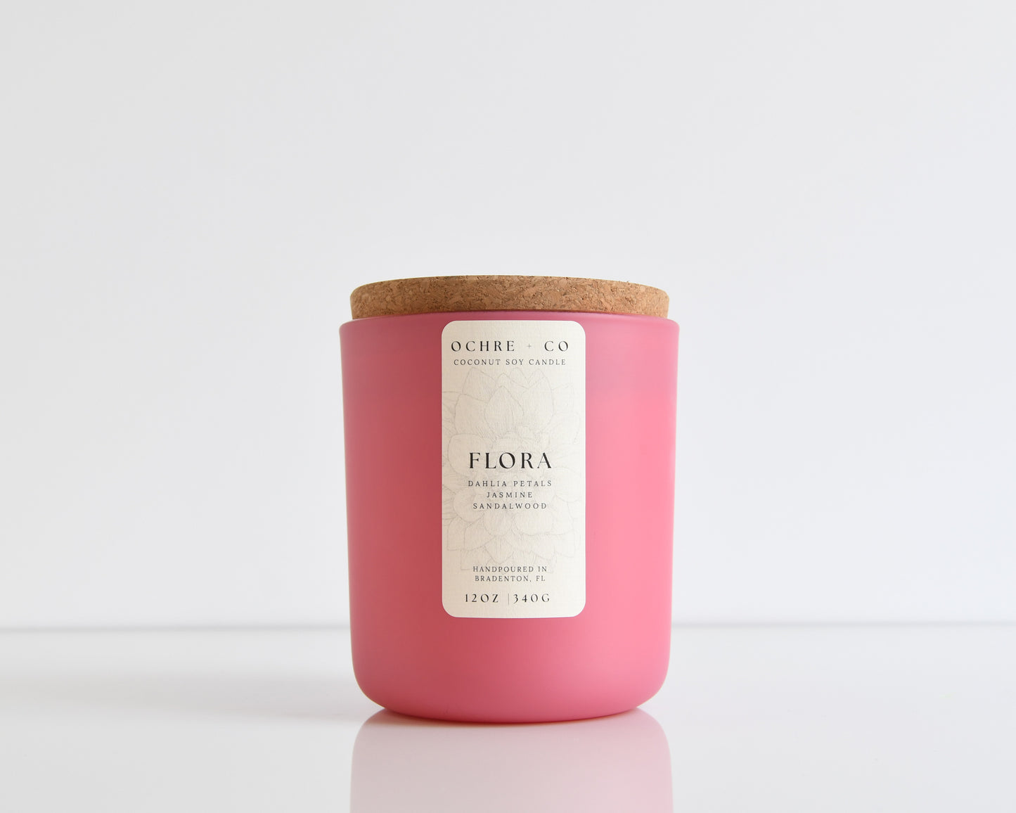 Scented candle labeled 'Flora' in a matte pink green vessel with a cork lid on a white background