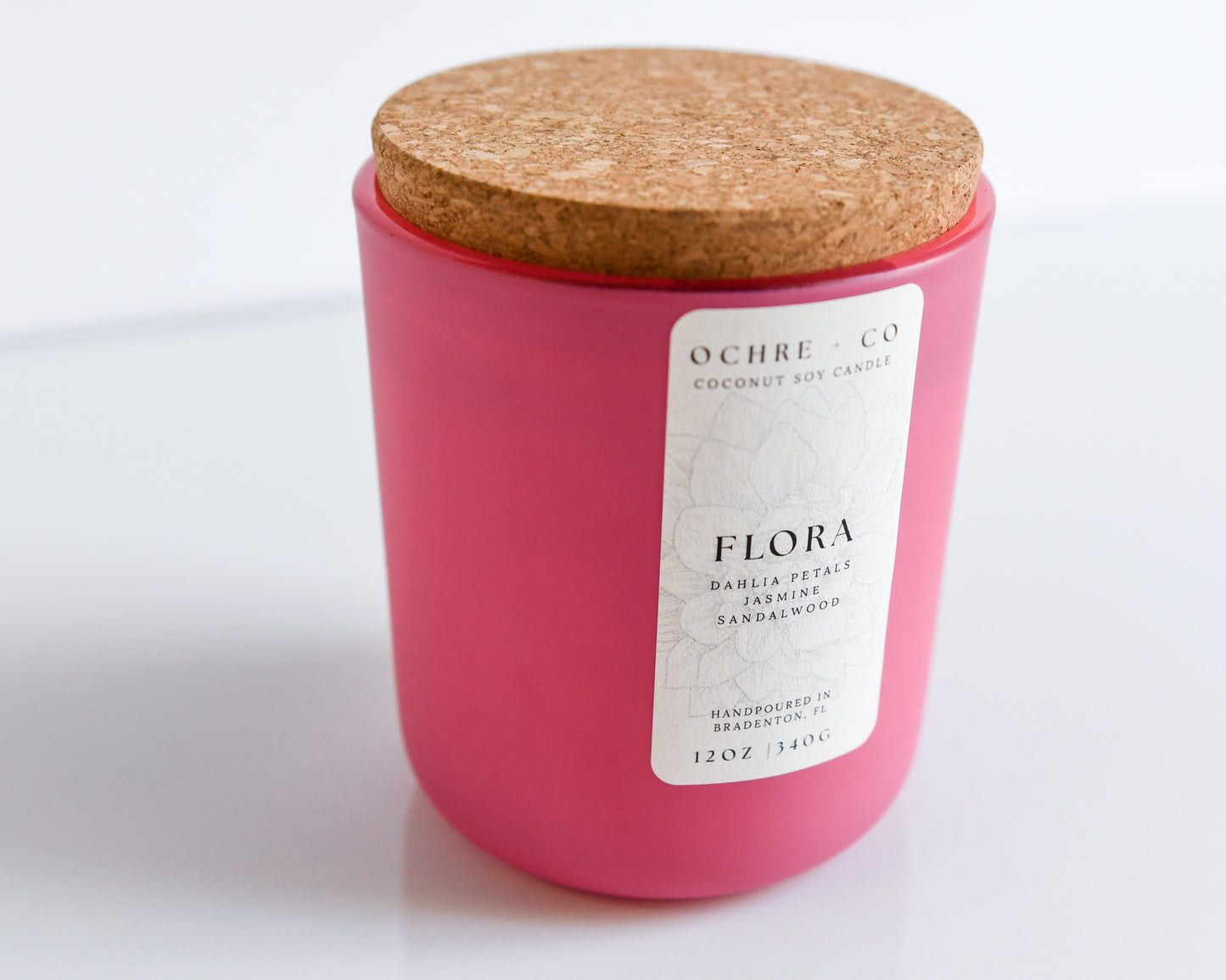 Scented candle labeled 'Flora' and 'Ochre & Co' label  in a matte pink vessel with a cork lid on a white background
