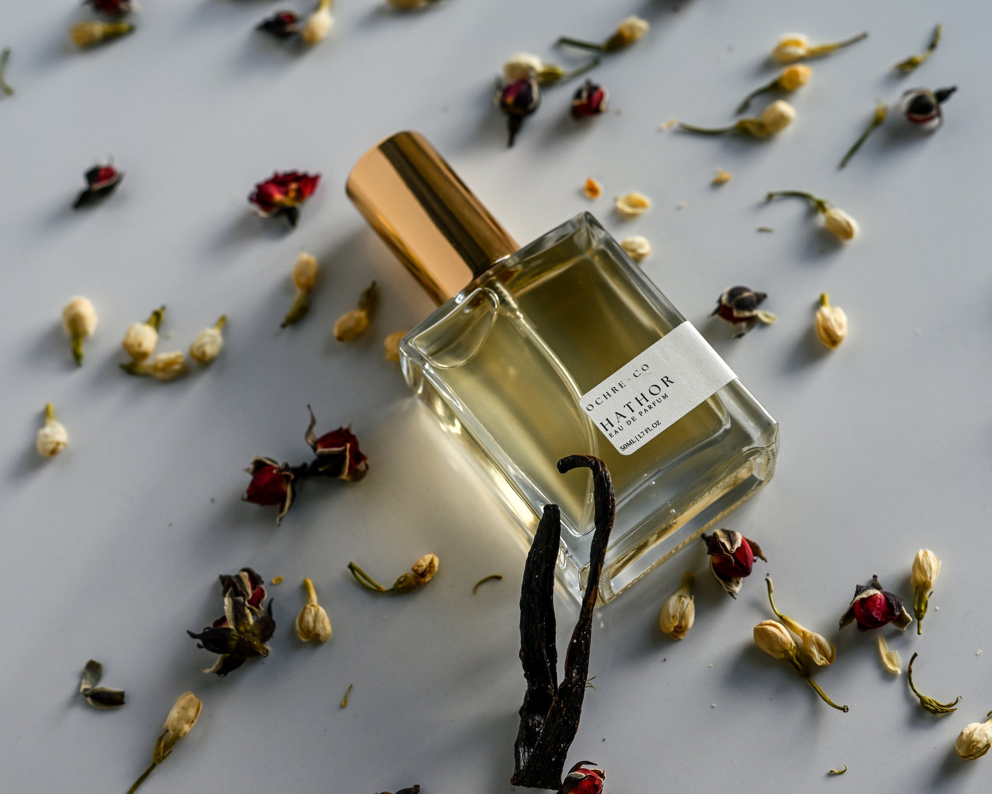 Perfume bottle of Hathor with dried flowers and vanilla bean on a light surface