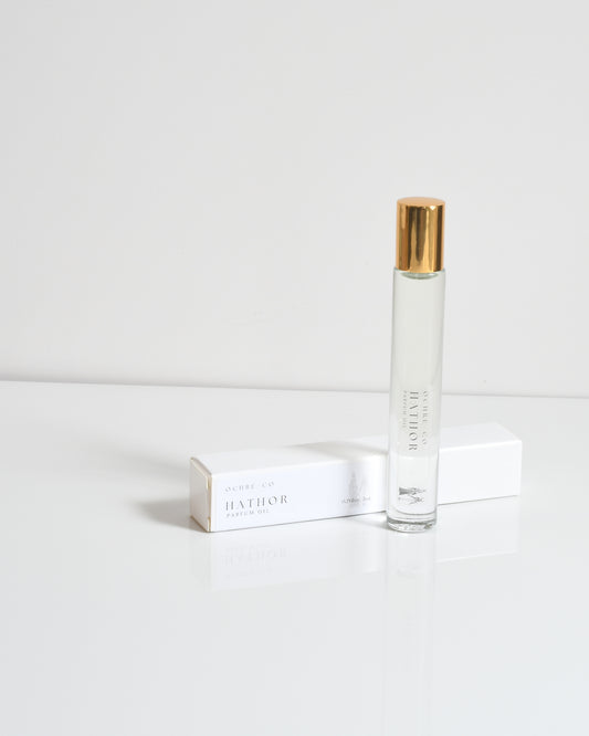 Hathor perfume oil bottle with a clear liquid and a gold cap, on a white surface.