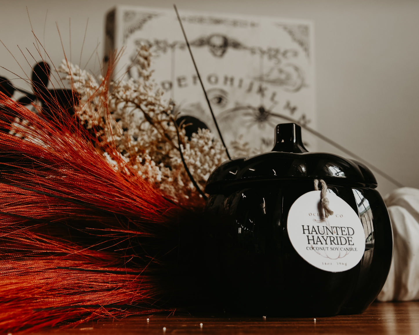 A black pumpkin-shaped ceramic candle vessel on a wooden countertop with orange and white florals