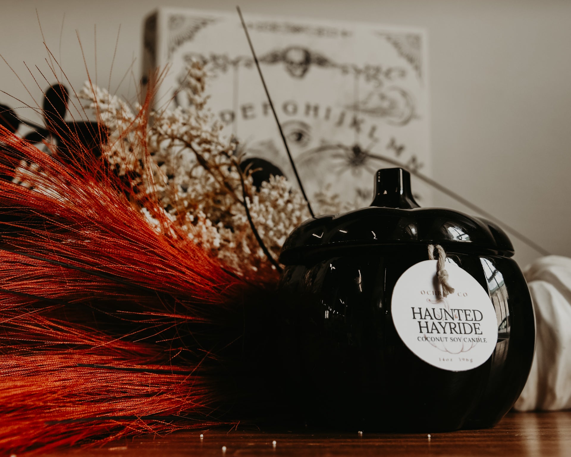 A black pumpkin-shaped ceramic candle vessel on a wooden countertop with orange and white florals