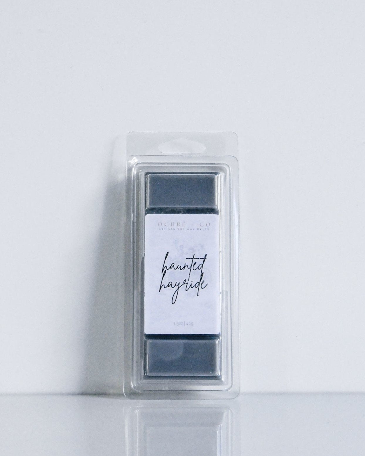 A black wax melt in a clear plastic packaging with a label that reads 'Haunted Hayride' by OCHRE + CO.