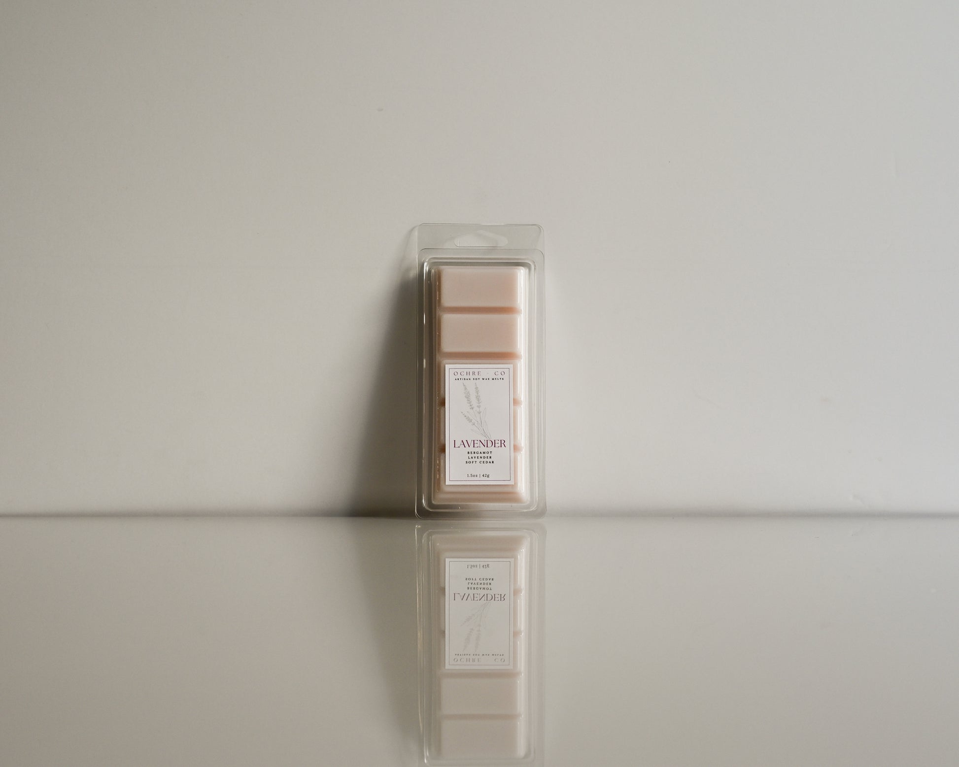 Packaged lavender wax melt on a reflective surface with a neutral background