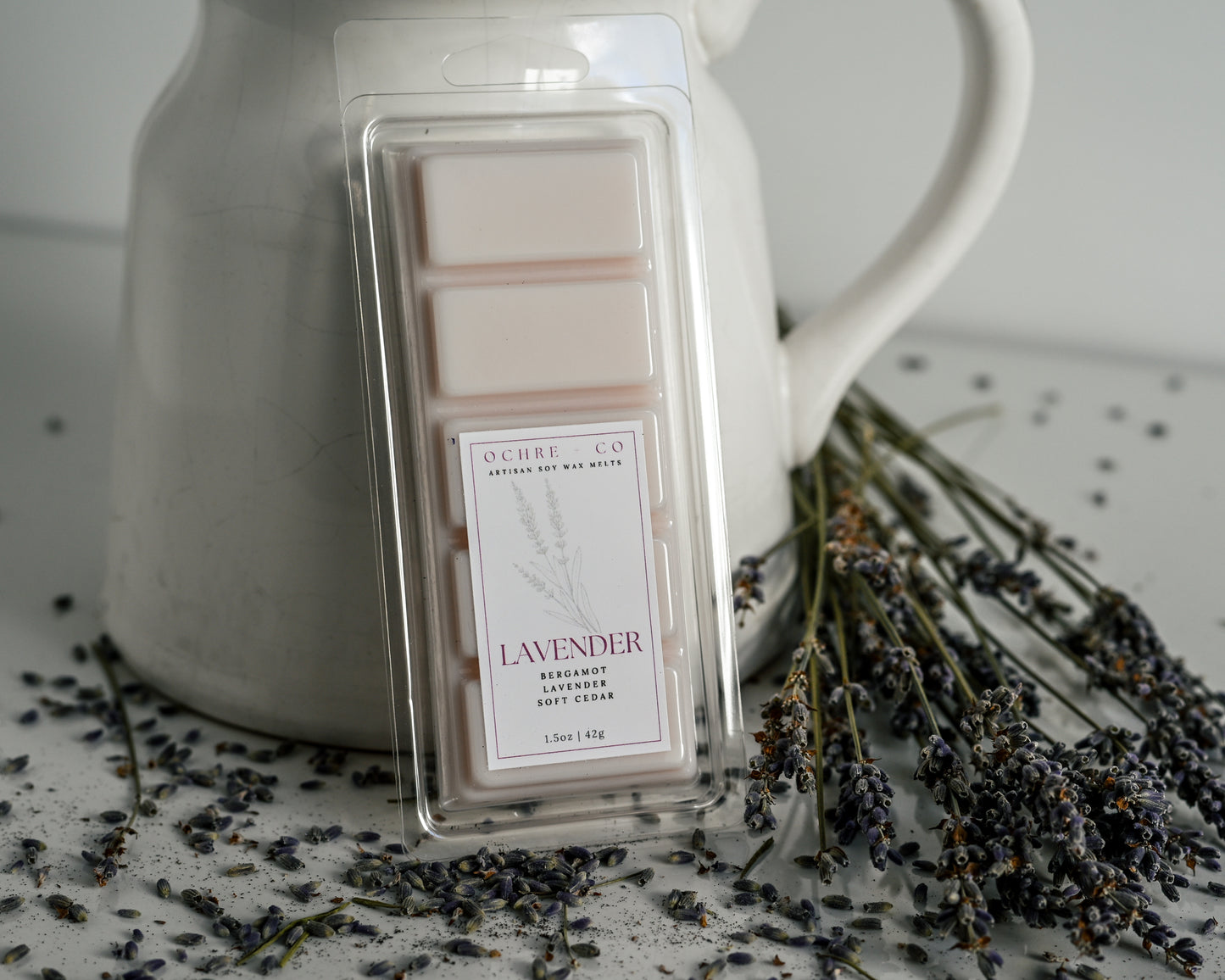 Olech & Co lavender wax melts in packaging with dried lavender flowers on a white surface.